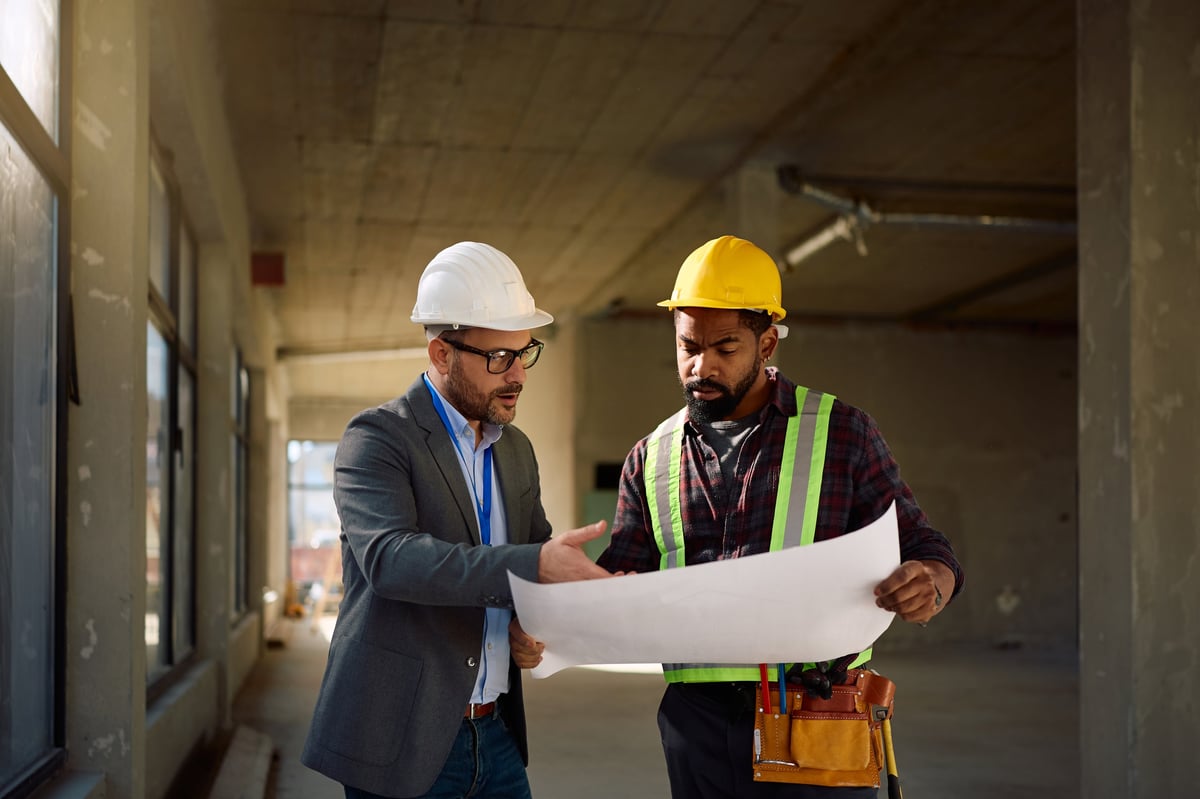 Building contractor going through blueprints with African American worker at construction site