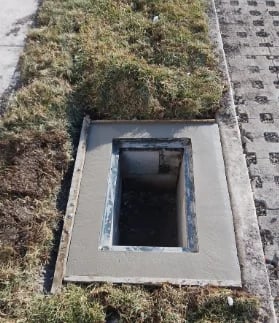 Overhead view of a roof vent or access hatch opening with dark interior, surrounded by moss and shingle roofing material