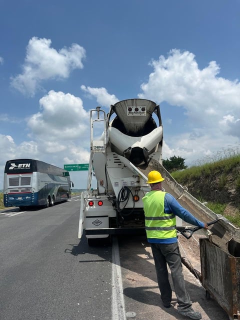 Construction worker in safety gear directing concrete mixer truck on highway during daytime
