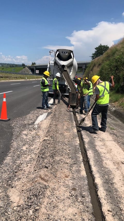 Concrete truck pouring cement into roadside trench with construction workers in safety gear supervising the work